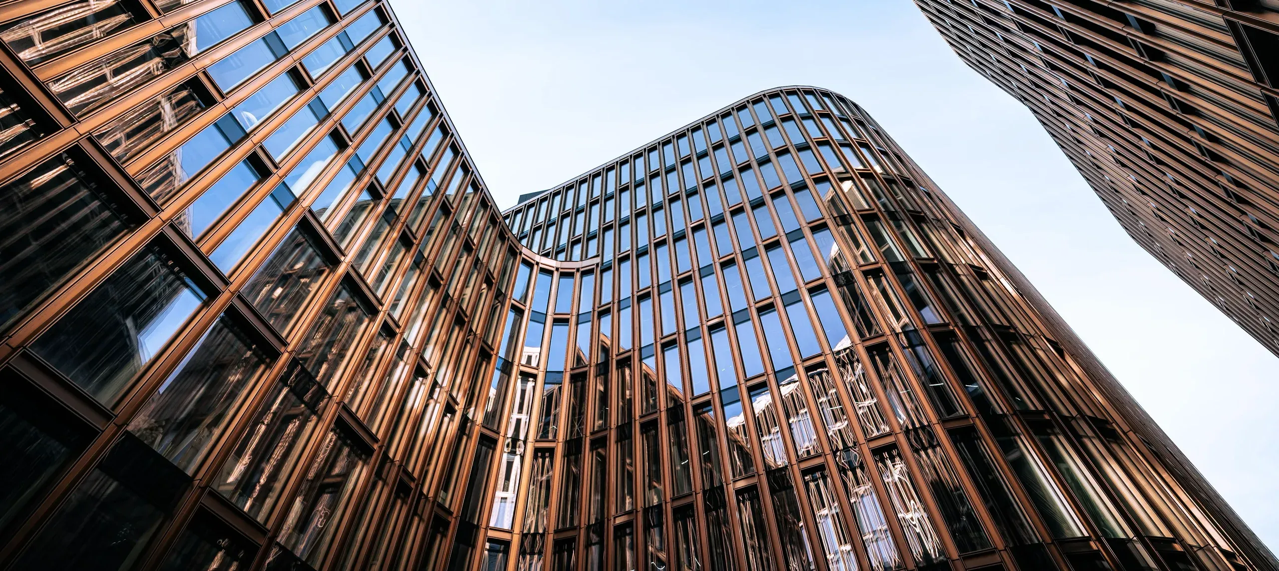 Fasaden på et næringsbygg sett nedenfra, med bronsefargede vertikale profiler og en buet glassfront mot himmelen